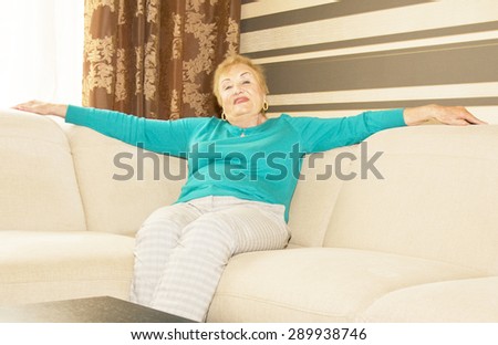 European lady in agis sitting on sofa at home and plate with apples.