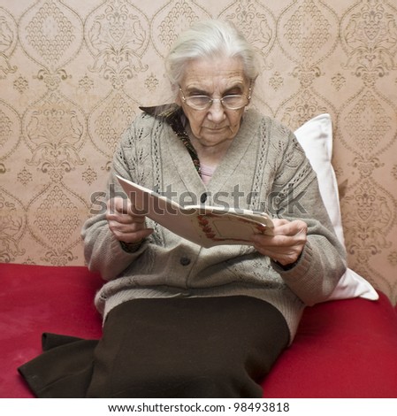 Old lady (European) sitting reading book at home.