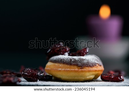 Delicious donut topped with chocolate and cranberries. Romantic atmosphere, candle in background. Shallow depth of field.