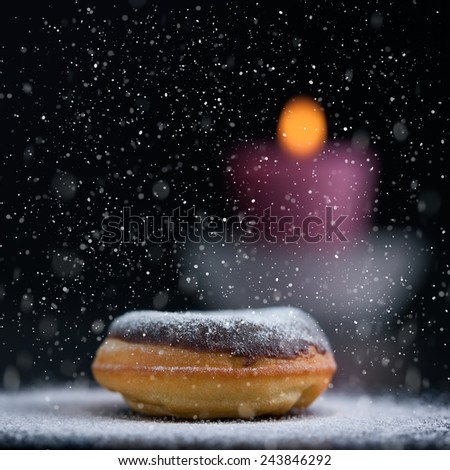 Sprinkling sugar on delicious donut topped with chocolate. Romantic atmosphere with candle in background. Shallow depth of field.