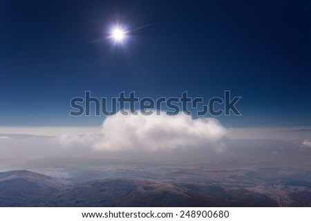 View from the top of the mountain towards the sun on illuminated lone cloud