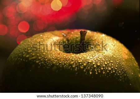 the big apple - a macro / close-up contrast shot of a top of a fresh wet green apple  covered with drops / dew and city lights / blurry red lights / spots on the background., while raining.