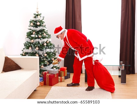 Senior man in Santa Claus uniform, putting a gift from bag under the decorated christmas tree