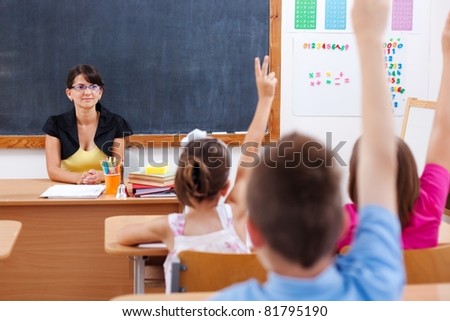Teacher sitting in classroom and looking at students who raised their arms