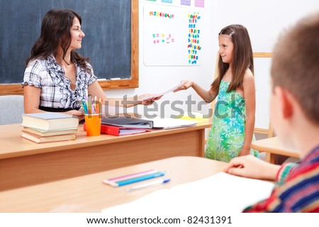 Schoolgirl standing in front of teacher, giving or receiving test paper