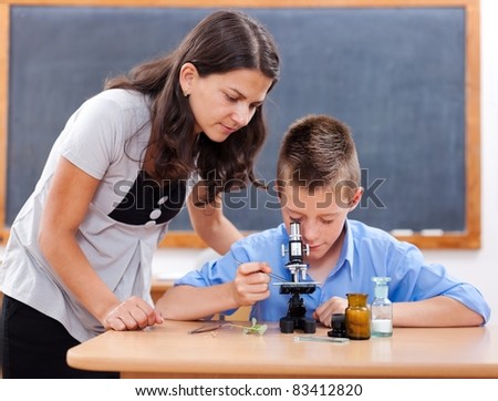 Schoolboy looking inot microscope while the biology teacher is attending him