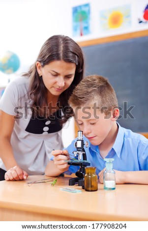 Teacher assisting schoolboy looking into microscope in biology class
