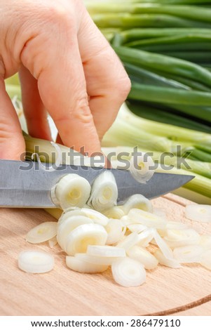 Macro of woman\'s hand cutting fresh scallion on wooden cutting board
