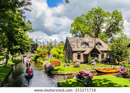 GIETHOORN, NETHERLANDS - AUGUST 13, 2013: Unknown visitors in the sightseeing boating trip in a canal in Giethoorn. The beautiful houses and gardening city is know as 