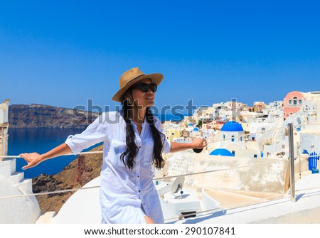 Happy Asian woman in sun hat enjoying her holidays on Santorini island, Greece. View on Caldera and Aegean sea from Oia, Santorini.
