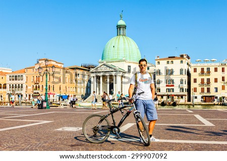 VENICE, ITALY- JULY 21: Tourist posing with bicycle in front of Train station Venezia Santa Lucia with Grand canal and Santa Maria Della Salute church on background in Venice, Italy on July 21, 2015.