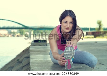 Woman stretching her leg by the river after running...