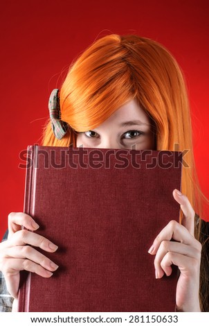 Closeup of young redhead woman peeking over the edge of the closed book