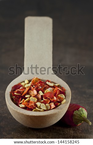 Wooden spoon with dried crushed chili red pepper and whole dried chili pepper on dark wood table background. Spicy food concept.