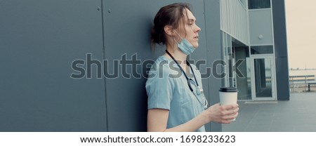 Portrait of tired exhausted nurse or doctor having a coffee break outside in the morning. COVID-19, Coronavirus pandemic