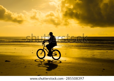 Silhouette soft focus guy riding bike on the beach.