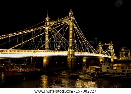 LONDON, UK - SEPTEMBER 16, 2013: Albert Bridge in London at night lit up with many lights and boats docked underneath on September 16 2013