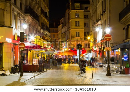 PARIS, FRANCE - 19TH MARCH 2014: A view down a street in Paris at night showing the blurred motion of people and restaurants, cafes and other shops