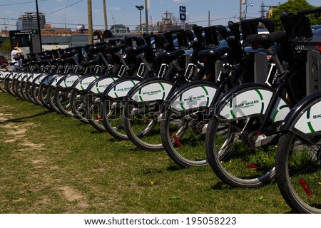 TORONTO, CANADA - 25TH MAY 2014: Rows of bikes at their docking stations for Torontos Bike Share. A lady can be seen at the payment terminal in the background.