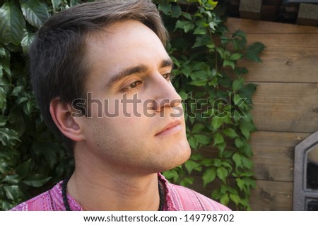 Head and shoulder portrait of a young man facing to the side out of a log cabin