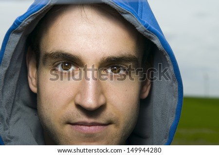 frontal head portrait of a young man with blue hood directly into the camera looking