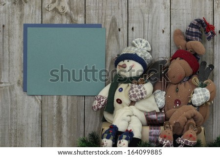 Snowman and moose sitting by fence with blank sign