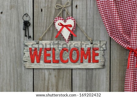 Red wood welcome sign with heart and iron keys hanging next to gingham curtain
