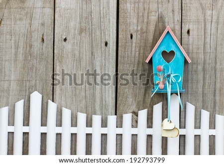 Teal blue birdhouse with wooden hearts hanging over white picket fence