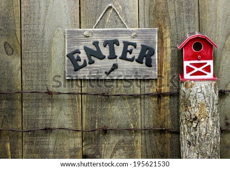 Enter sign over barbed wire fence next to post with red barn birdhouse