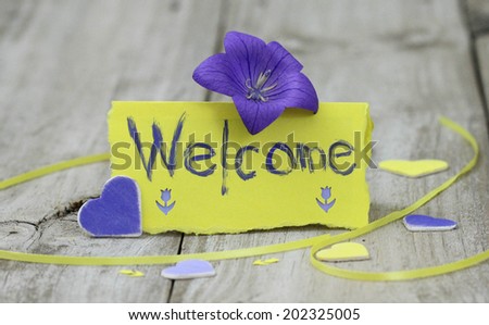 Welcome note card on wood table with purple flowers and hearts