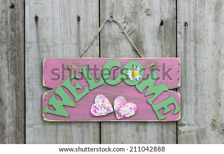 Weathered pink welcome sign with flowers and hearts hanging on wooden door