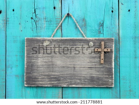 Blank weathered sign with wooden cross hanging by rope on antique teal blue wood door