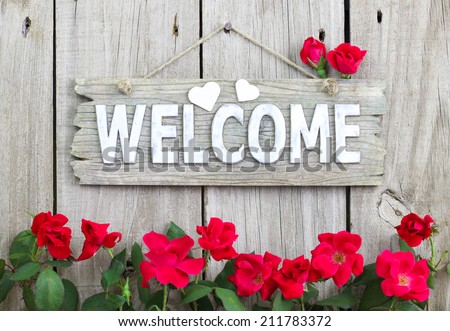 Weathered welcome sign with hearts hanging on wood fence with flower border of red roses