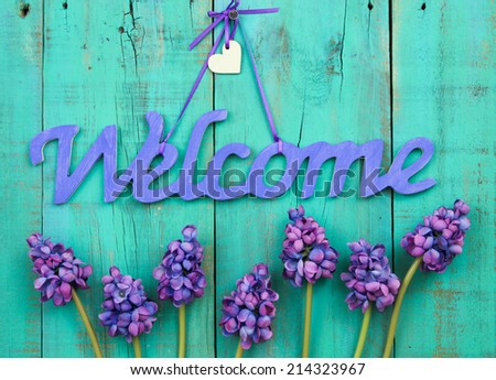 Purple welcome sign with flower border and wooden heart hanging on antique rustic green wood door
