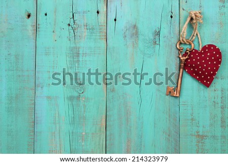 Bronze skeleton key and red heart hanging on antique teal blue weathered wood door