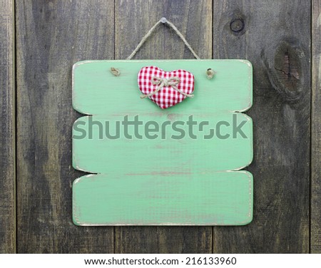 Blank green sign with red checkered heart hanging on rustic wood door