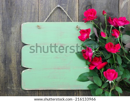 Distressed blank green sign with flower border of red roses hanging on rustic wood background