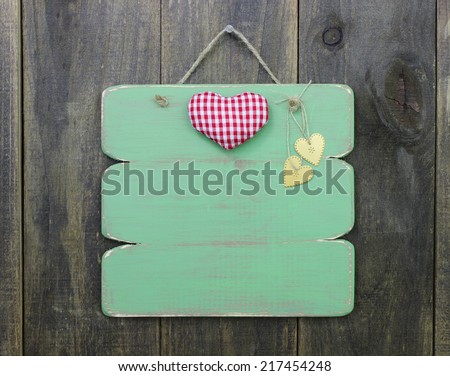 Red checkered and gold hearts on blank green sign hanging on rustic wooden door