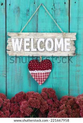 Wood welcome sign with country heart hanging over flowers on antique teal blue wooden fence