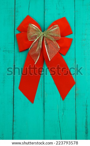 Red velvet and gold Christmas bows hanging on antique teal blue rustic wood door