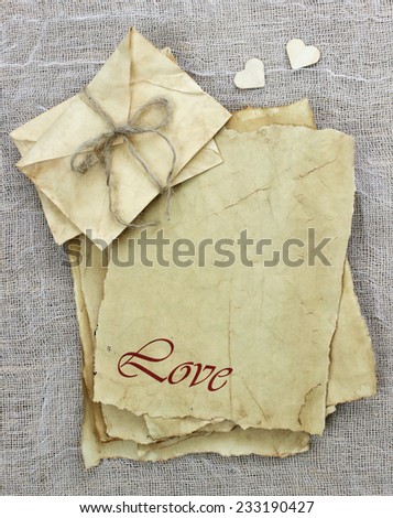 Love letter and envelopes tied in rope made of antique worn parchment paper on old burlap and white netting background with wooden hearts