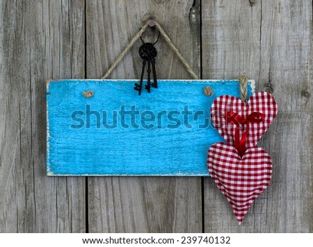 Blank antique teal blue sign with red fabric hearts and iron keys hanging on rustic wooden door