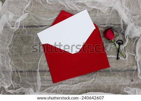 Blank white love letter or note card with red envelope, red flower and black iron key on shabby white netting and wood background