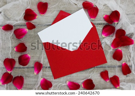 Blank white letter or note card and red envelope with red flower petals on shabby white netting and wood background