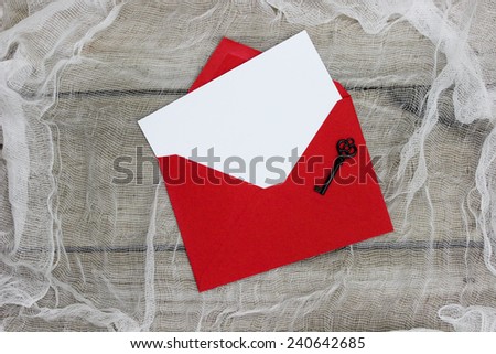 White note card or letter and red envelope with black iron key on shabby textured background