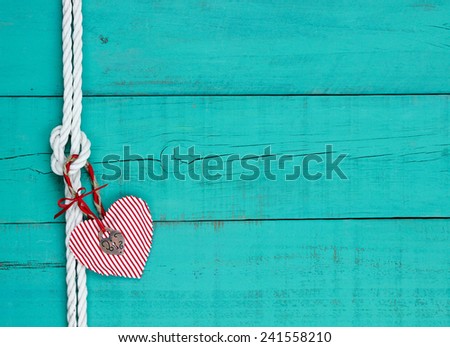 Red and white candy cane striped heart and silver lock hanging on rope with knot against blank antique teal blue rustic wooden background