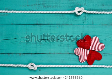 Red hearts border on blank antique teal blue wooden background with white rope with knots