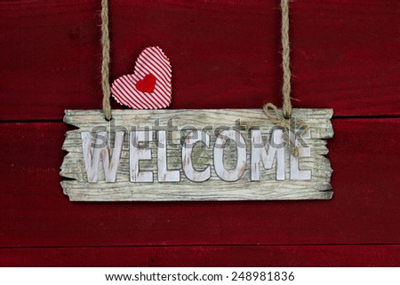 Wood welcome sign with red fabric hearts hanging on antique red wooden background