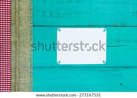 Blank white sign on antique teal blue wood background with red and white gingham, burlap and rope border