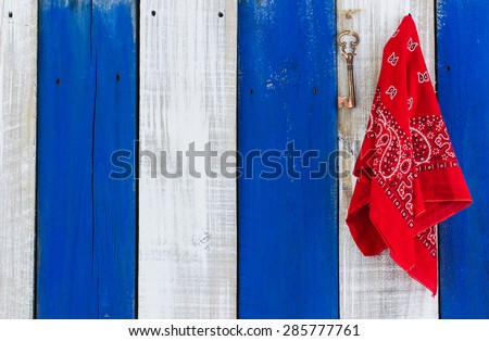 Red handkerchief or bandana and bronze skeleton key hanging on blue and white rustic wooden background